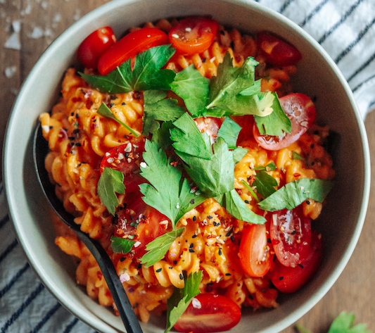 Nudeln in Schüssel mit roter Soße aus Paprika mit Tomaten und Koriander